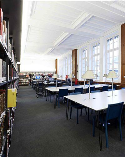 Salle de lecture avec grandes tables blanches, chaises bleues et étagères de livres