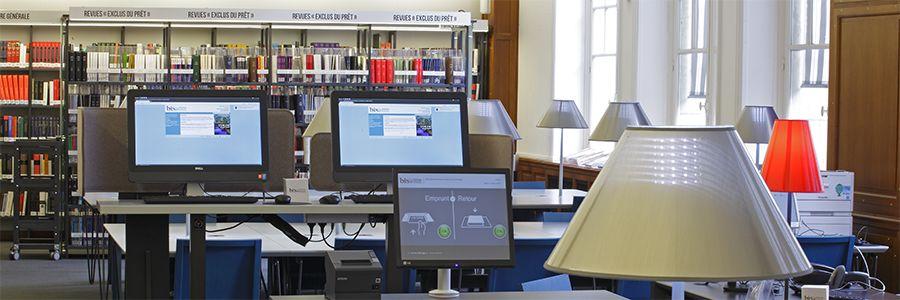 Deux ordinateurs sur tables en hauteur dans une salle de bibliothèque